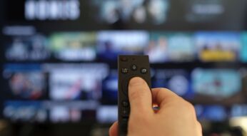 Hand hält eine Fernbedienung vor einen Fernseher