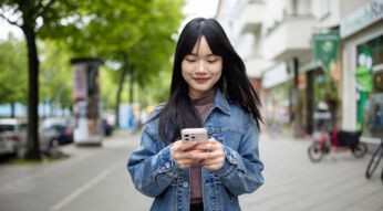 Eine junge Frau nutzt ihr Handy, während sie auf einem Bürgersteig steht