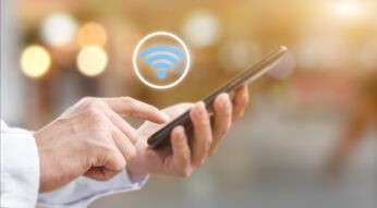 Nahaufnahme einer Hand, die ein Smartphone bedient. Darüber schwebt ein WLAN-Symol.