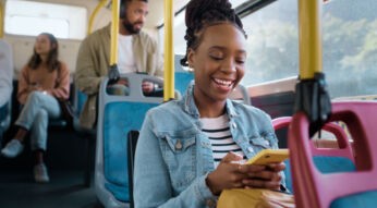 Eine junge Frau schaut im Bus auf ihr Smartphone und lächelt.