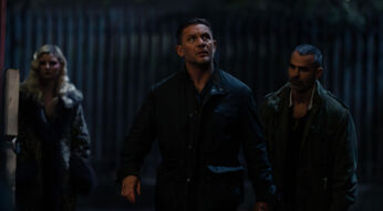 Auf dem Bild zur Mobland Serie ist Tom Hardy als Harry Da Souza zu sehen. Er steht in einer dunklen Gasse und blickt angespannt nach oben, als ob er eine Bedrohung wahrnimmt. Er trägt eine dunkle Jacke, und sein Gesichtsausdruck wirkt fokussiert. Hinter ihm stehen zwei weitere Personen – eine Frau mit blondem Haar in einem auffälligen Mantel und ein Mann mit kurz rasiertem Haar und einem ernsten Blick. Die Szene ist düster beleuchtet und vermittelt eine gespannte Atmosphäre.