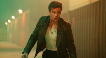 Auf dem Bild aus der Mr. No Pain Kritik ist Jack Quaid als Nathan Cain zu sehen. Er trägt eine schwarze Lederjacke über einem blutbefleckten weißen Unterhemd und wirkt erschöpft sowie alarmiert. Sein Gesicht ist mit Blutspuren bedeckt, und er scheint sich in einem beleuchteten Containerlager zu befinden. Die düstere Atmosphäre und sein angespannter Ausdruck deuten auf eine dramatische Szene voller Action hin.