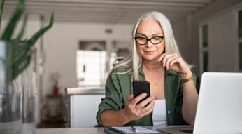 Eine Frau sitzt an einem Tisch und hält ein Smartphone in der Hand.