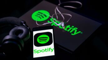 Das Spotify-Logo ist auf einem Smartphone und einem Tablet zu sehen, die neben einem Kopfhörer liegen.
