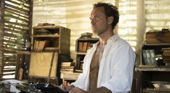 Jude Law verkörpert in Eden den Charakter Dr. Friedrich Ritter und ist hier an einer Schreibmaschine zu sehen, umgeben von Holzmöbeln und alten Büchern. Der konzentrierte Blick und die schlichte Umgebung spiegeln die isolierte und intellektuell geprägte Persönlichkeit wider, die im Zentrum der Eden wahre Geschichte steht.