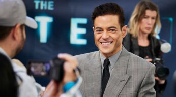 Auf dem Bild zur Premiere von The Amateur ist Schauspieler Rami Malek zu sehen. Er trägt ein elegantes, kariertes Sakko mit Krawatte und lächelt in die Kamera, während im Hintergrund Medienvertreter mit Kameras zu sehen sind. Das Bild gehört zu einer Liste der besten Filme von Rami Malek.