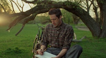 GigaTV-Highlights im April 2025: In einer Szene aus The Brutalist sitzt Adrien Brody als zurückhaltender Architekt in einem ruhigen Park auf dem Gras und schreibt in ein Notizbuch.