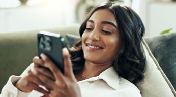 Frau liegt auf der Couch und surft am iPhone.