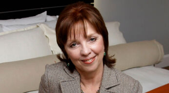 Nora Roberts posiert auf einem Bett in einem Hotelzimmer.