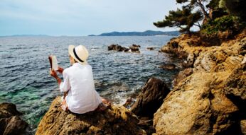 Eine Frau liest an einer felsigen Küste ein Buch