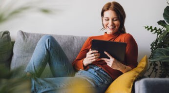 Eine Frau sitzt auf einem Sofa und benutzt ein Tablet.