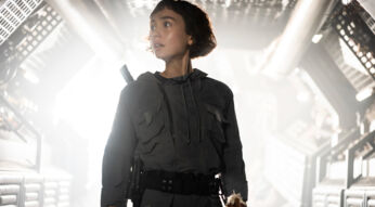 In dieser Szene aus der Alien: Earth Serie steht Wendy, gespielt von Sydney Chandler, in einem futuristischen Raumschiffkorridor. Sie trägt einen dunklen Kampfanzug mit taktischem Gürtel, wirkt angespannt und blickt nach links.