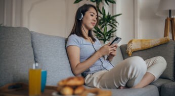 Eine Frau sitzt auf dem Sofa und hört über Kopfhörer Musik vom Android-Smartphone.