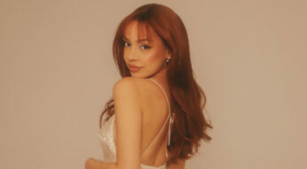 Für den Artikel über ayliva tickets zeigt das Bild Sängerin Ayliva mit rotbraunen, offenen Haaren und einem hellen, schimmernden Top mit dünnen Trägern. Sie blickt über die Schulter zur Kamera, vor einem neutralen, beigen Hintergrund.