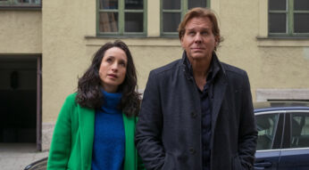 Das Artikelbild zu den Der Alte-Darsteller:innen zeigt Thomas Heinze als Hauptkommissar Caspar Bergmann (rechts) und Stephanie Stumph als Kommissarin Annabell Lorenz (links) nebeneinander in einem Innenhof. Beide blicken nachdenklich nach oben. Heinze trägt einen dunklen Mantel, Stumph einen auffälligen grünen Mantel über einem blauen Pullover.