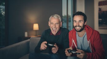 FRITZ!Box Ping verbessern: Zwei Männer sitzen auf einer Couch und halten PlayStation Controller in der Hand.