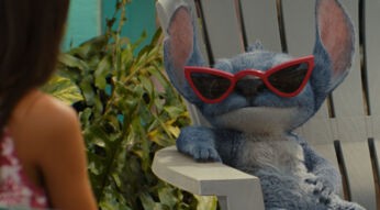 Stitch sitzt auf einem Holzstuhl und trägt eine Sonnenbrille.