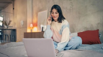 Vodafone Kabel-Internet- & Telefon-Anschluss freischalten: Frau sitzt telefonierend vor ihrem Laptop auf dem Bett.