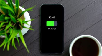 Im Artikel iphone-Akku tauschen zeigt dieses Bild ein modernes iPhone mit schwarzem Display auf einem dunklen Holztisch. Der Bildschirm zeigt 82 Prozent Akkuladung.