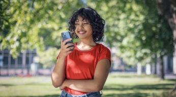 Plötzlich hoher Datenverbrauch: junge Frau schaut lächelnd auf ihr Handy in einem Park.