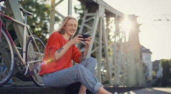 Roaming Xiaomi funktioniert nicht: junge Frau sitzt auf einer Brücke lächelnd neben ihrem Farrahd und schaut auf ihr Handy