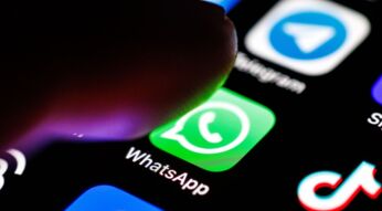 Das WhatsApp-Logo ist auf dem Display eines Smartphones zu sehen, während sich ein Zeigefinger dem App-Symbol nähert.