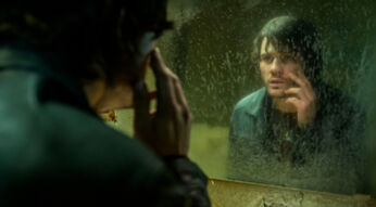 In dieser Szene aus den Spieleverfilmungen 2026 ist James Sunderland, gespielt von Jeremy Irvine, vor einem schmutzigen Spiegel zu sehen. Er betrachtet sich nachdenklich und leicht verstört, während er mit der Hand sein Gesicht berührt. Die düstere Stimmung und das heruntergekommene Badezimmer deuten auf psychische Belastung und innere Konflikte hin.