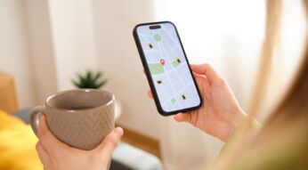 Frau mit Tasse in der Hand schaut auf die Navigations-App auf ihrem iPhone.