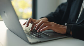 Auf dem Bild mit symbolischem Bezug zu Perplexity Pro ist eine Person in Business-Kleidung zu sehen, die konzentriert auf einem modernen Laptop tippt. Die Szene wirkt professionell und fokussiert, im Hintergrund ist ein Fenster mit natürlichem Licht und unscharfem Ausblick zu erkennen. Am Handgelenk trägt die Person eine Smartwatch.