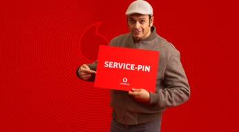 Kaya Yanar ist auf dem Bild zur Vodafone Service-PIN Kampagne zu sehen, wie er ein rotes Schild mit der Aufschrift „SERVICE-PIN“ hält und darauf zeigt.