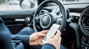 Eine Person sitzt im Auto und bedient ihr Smartphone.