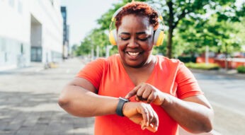 Eine Frau mit Kopfhörern bedient lächelnd ihre Apple Watch