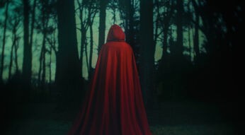 Dieses Symbolbild zur Alchemised Verfilmung zeigt Helena als abstrakte Figur in einem langen, tiefroten Umhang. Sie steht mit dem Rücken zur Kamera in einem dunklen Wald. Die Inszenierung erzeugt eine geheimnisvolle, atmosphärisch verdichtete Stimmung, die Helenass innere Reise sinnbildlich widerspiegelt.