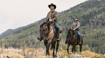 In dieser Szene aus der Marshals Serie sind Luke Grimes als Kayce Dutton und Logan Marshall-Green als Pete Calvin auf Pferden in einer bergigen, waldreichen Landschaft unterwegs. Beide tragen lässige Westernkleidung mit ernsten Gesichtsausdrücken. Die Stimmung wirkt ruhig, aber gespannt – typisch für ein modernes Western-Drama.