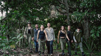 Auf dem Bild zu 7 vs. Wild Gewinner:innen sind sieben Teilnehmende im Dschungel zu sehen. Von links nach rechts: Jeannine Michaelsen, Joe Vogel, Fibii, Lucas „Avive“ Michels, Imke Salander, Kris Grippo und David Leichtle. Alle tragen Outdoor-Kleidung und wirken fokussiert und entschlossen, während sie durch dichtes Grün marschieren.