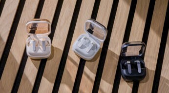 Drei Ausführungen der Kopfhörer Galaxy Buds4 Pro im Ladecase liegen auf einem Holztisch.