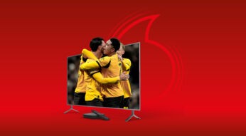 Auf dem Werbebild zur BVB-Mediathek ist ein Fernseher vor rotem Hintergrund abgebildet, auf dessen Bildschirm mehrere BVB-Spieler in gelben Trikots zu sehen sind, die sich umarmen. Unten ist eine Fernbedienung vor dem Fernseher platziert.