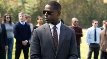 Special Agent Xavier Collins aus „Paradise“ steht im grauen Anzug mit Sonnenbrille auf einer Wiese, mehrere Personen sind unscharf im Hintergrund zu sehen.