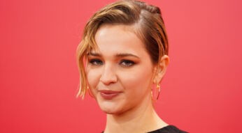 Auf diesem Porträt zur möglichen Struwwelpeter-Serie ist die Schauspielerin Lisa Vicari vor einem kräftig roten Hintergrund zu sehen. Sie trägt ein schwarzes Oberteil und goldene Creolen. Ihr kurzes blondes Haar ist seitlich gestylt, eine Strähne fällt locker ins Gesicht. Ihr Blick wirkt ruhig und selbstbewusst, wodurch die Nahaufnahme eine konzentrierte und leicht nachdenkliche Stimmung erzeugt.