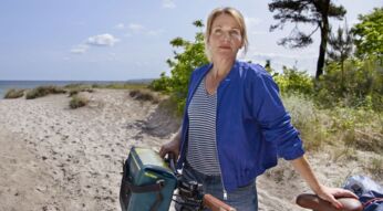 Tanja Wedhorn als Nora Kaminski in "Praxis mit Meerblick" am Strand mit einem Fahrrad.