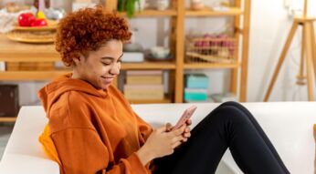Eine junge Frau sitzt auf dem Sofa und surft auf dem Handy im Internet.