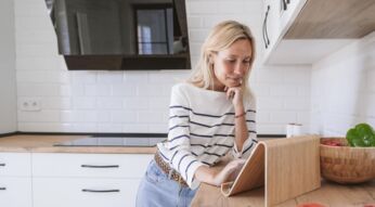 Eine junge Frau arbeitet in der Küche auf ihrem Tablet-PC.