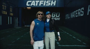 Glen Powell als Chad Powers mit blonder Perücke und Sonnenbrille steht mit Trainerin im „Catfish“-Tunnel Staffel 2 auf Disney+.