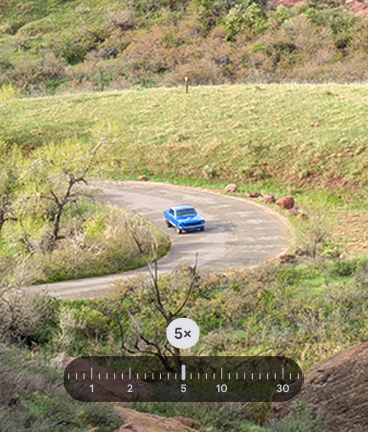 Ein blauer Oldtimer auf einer kurvenreichen, asphaltierten Strae durch eine grn-braune Hgellandschaft