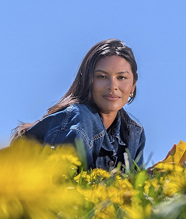 Eine Frau liegt in einem Feld mit gelben Blumen und lchelt in die Kamera