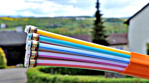 Nahaufnahme von Glasfaser-Kabeln, dahinter ein Wohngebiet.