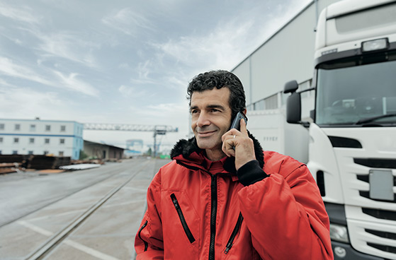 Ein Herr steht vor seinem LKW und telefoniert mit dem Handy