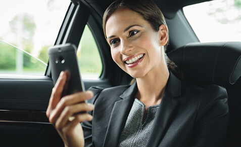 Frau schaut im Auto auf ihr Smartphone und nutzt den Selbständigen-Vorteil. Sie nutzt die Roaming-Optionen aus dem Privatkunden-Bereich.