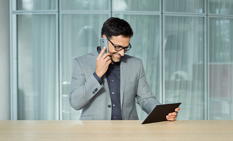 Mann mit Business-Smartphone am Ohr schaut auf ein Tablet. Er nutzt die GigaKombi Business.