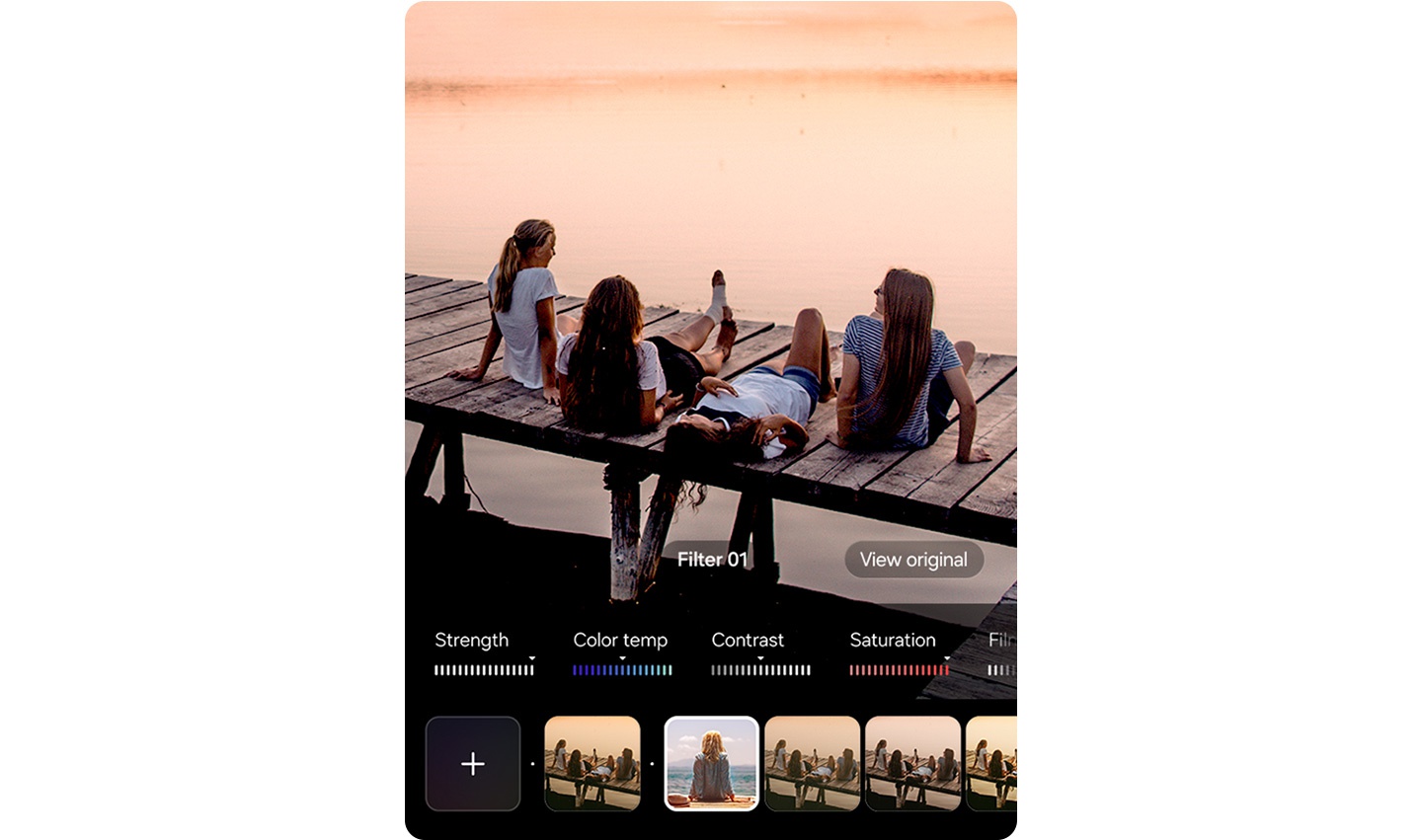 Vier Personen sitzen bei Sonnenuntergang auf einem Holzsteg an einem Gewsser. Am unteren Display-Rand ist eine Bearbeitungsoberflche mit Schiebereglern fr Intensitt, Farbtemperatur, Kontrast und Sttigung sowie Filteroptionen zu sehen, von denen eine in der Mitte ausgewhlt ist.